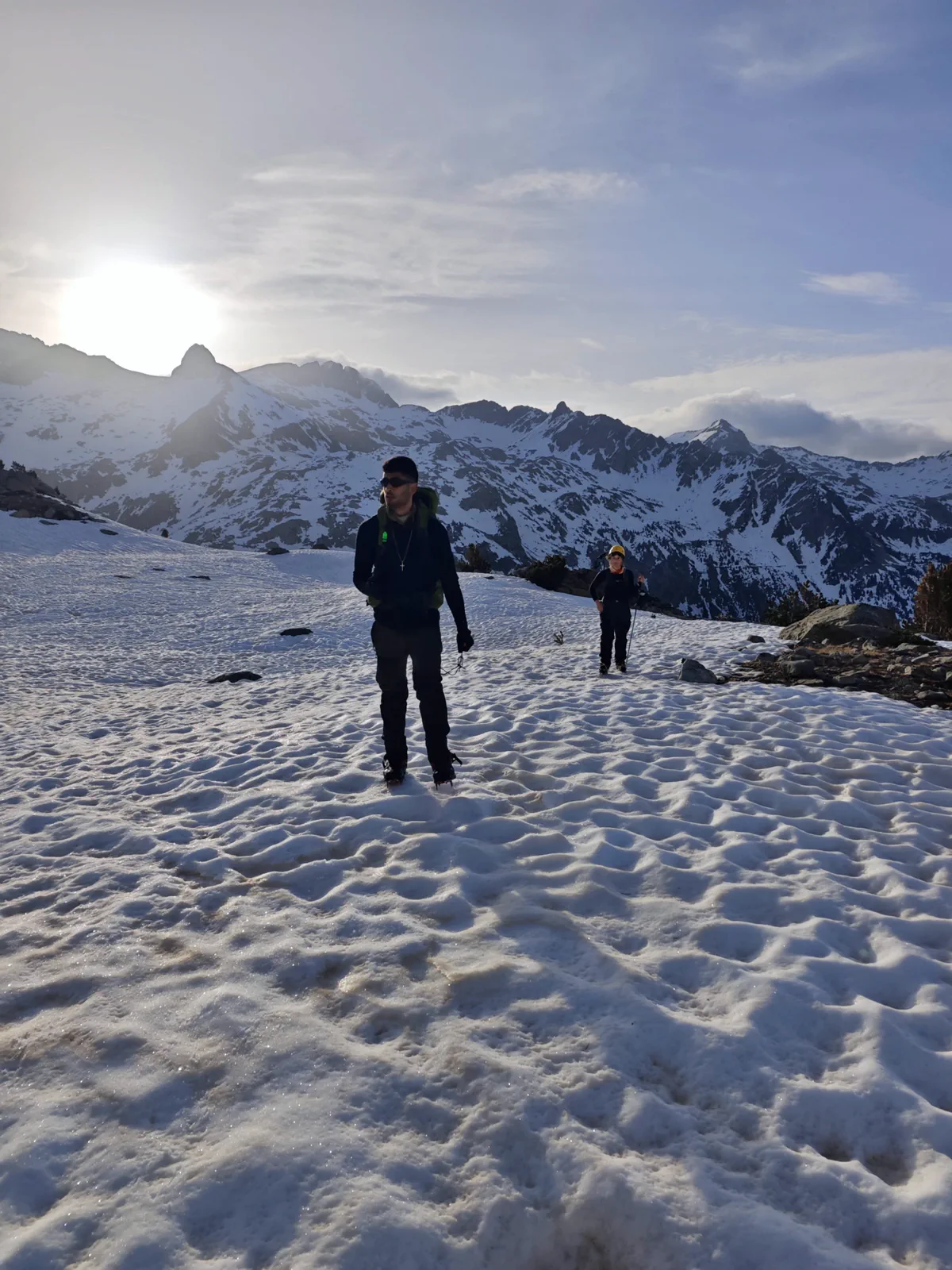 Two mountaineers cross the snow with the peaks behind them