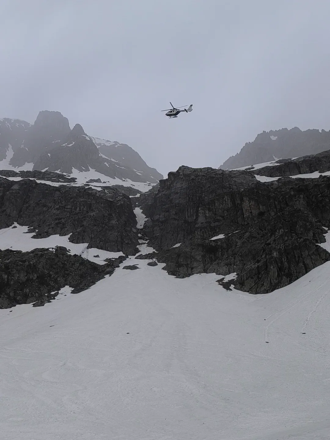 Rescue helicopter above a cloud-covered mountain cirque