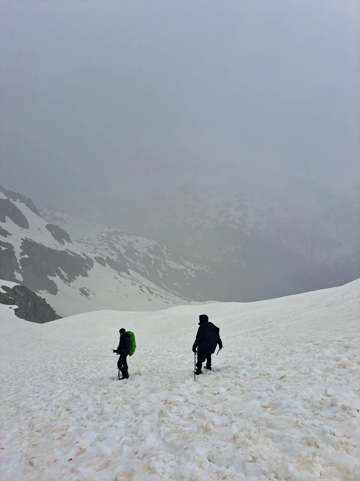 Two group members progress through the snow in poor visibility