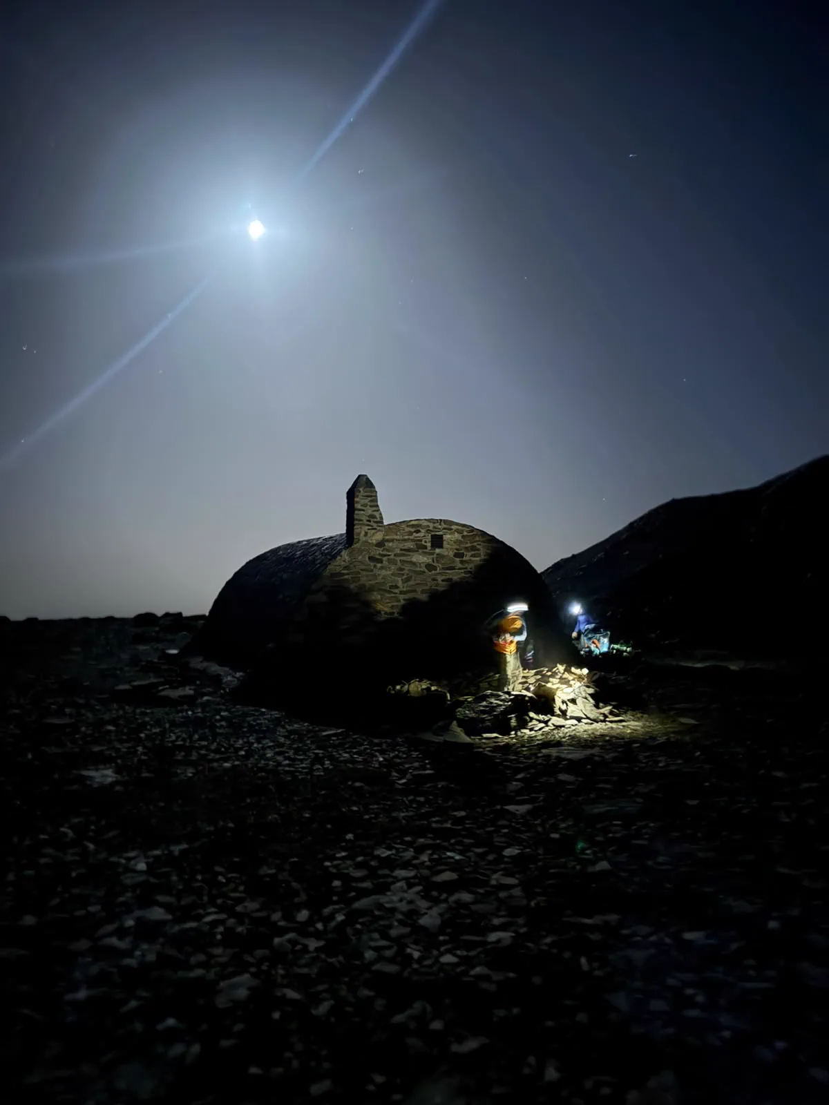 A stone shelter lit during a night bivouac