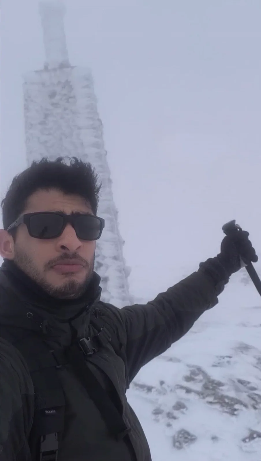 Self-portrait beside the ice-covered summit cairn in the mist