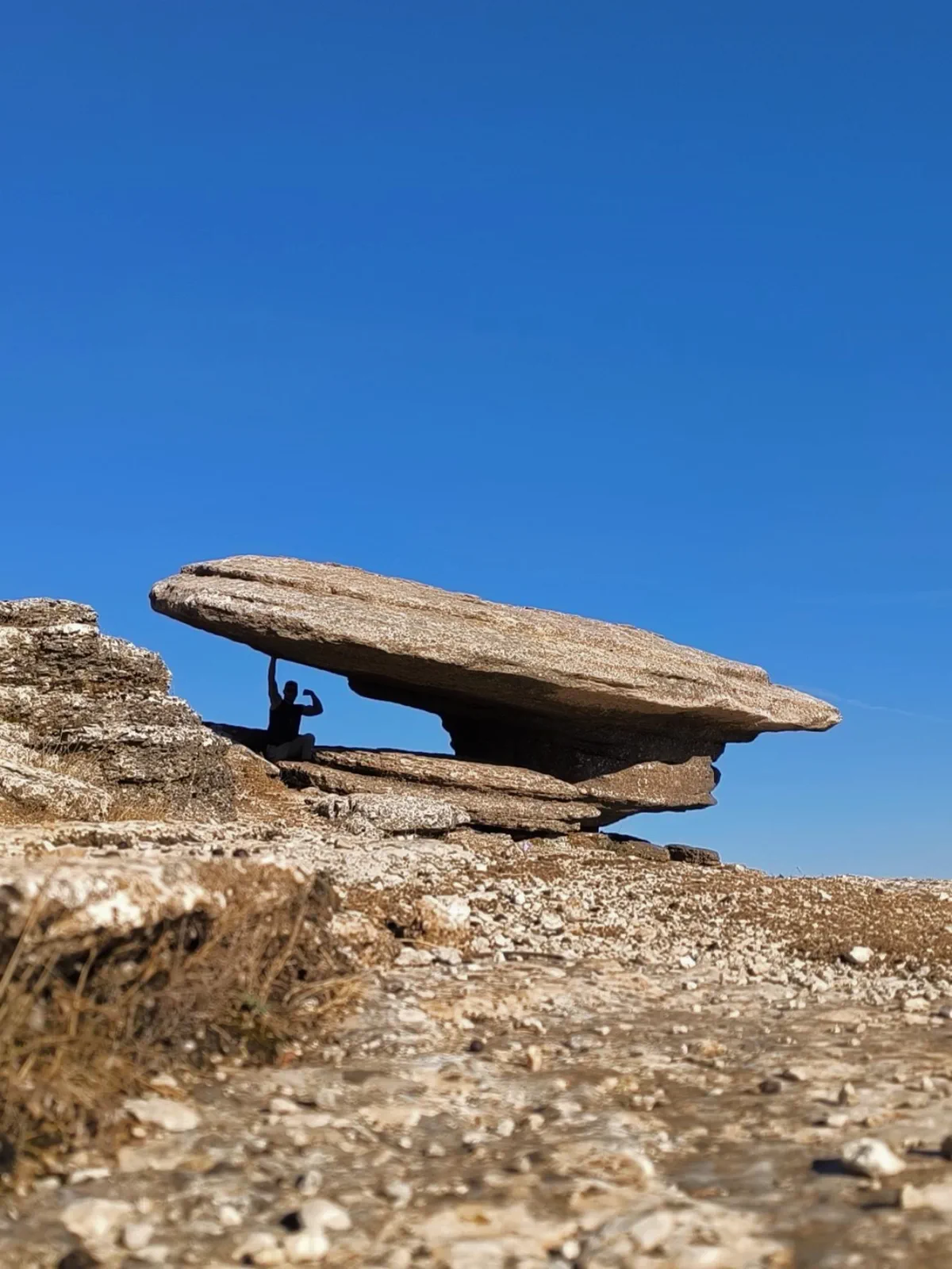 Large flat rock apparently balancing beneath a blue sky